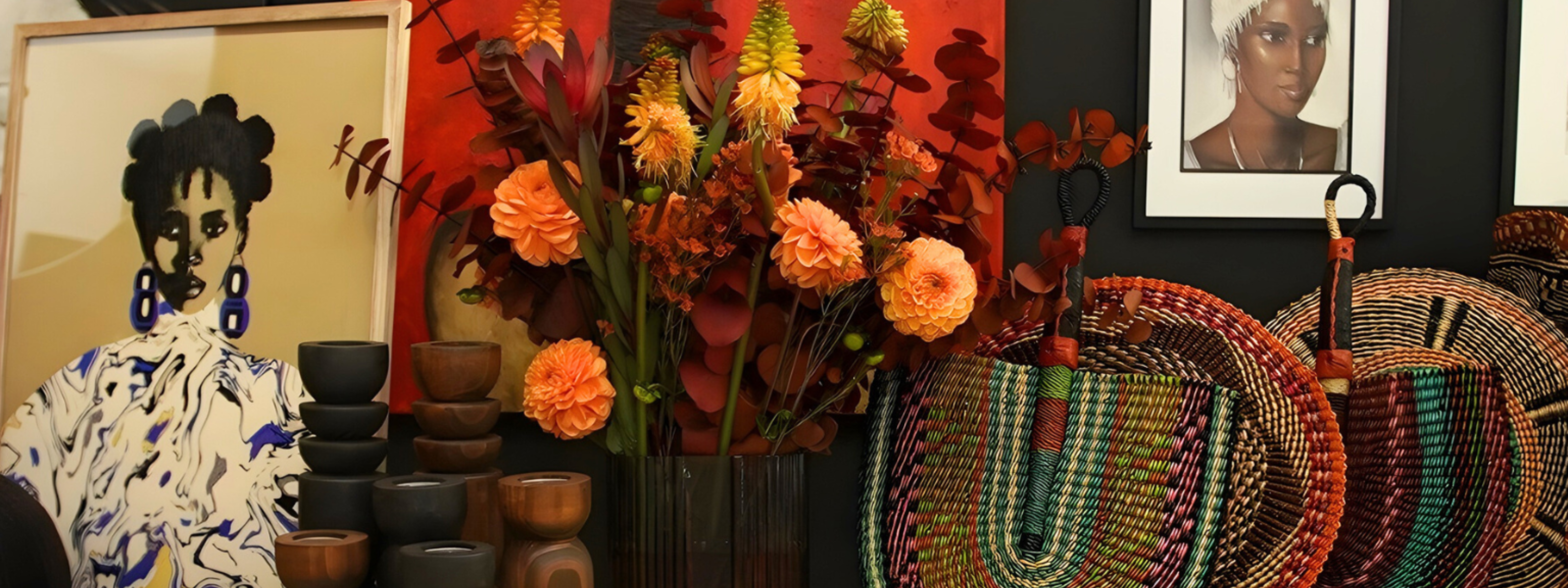 Fall flowers in red and orange with a portrait of a black woman in a geometric dress and bolga fans set on a dining table.