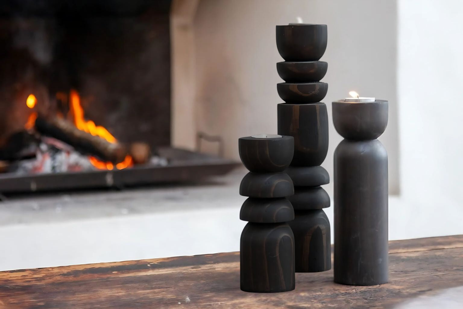 A set of 3 candle holders in small, medium and large sizes on a stool beside a bathtub in a bathroom.