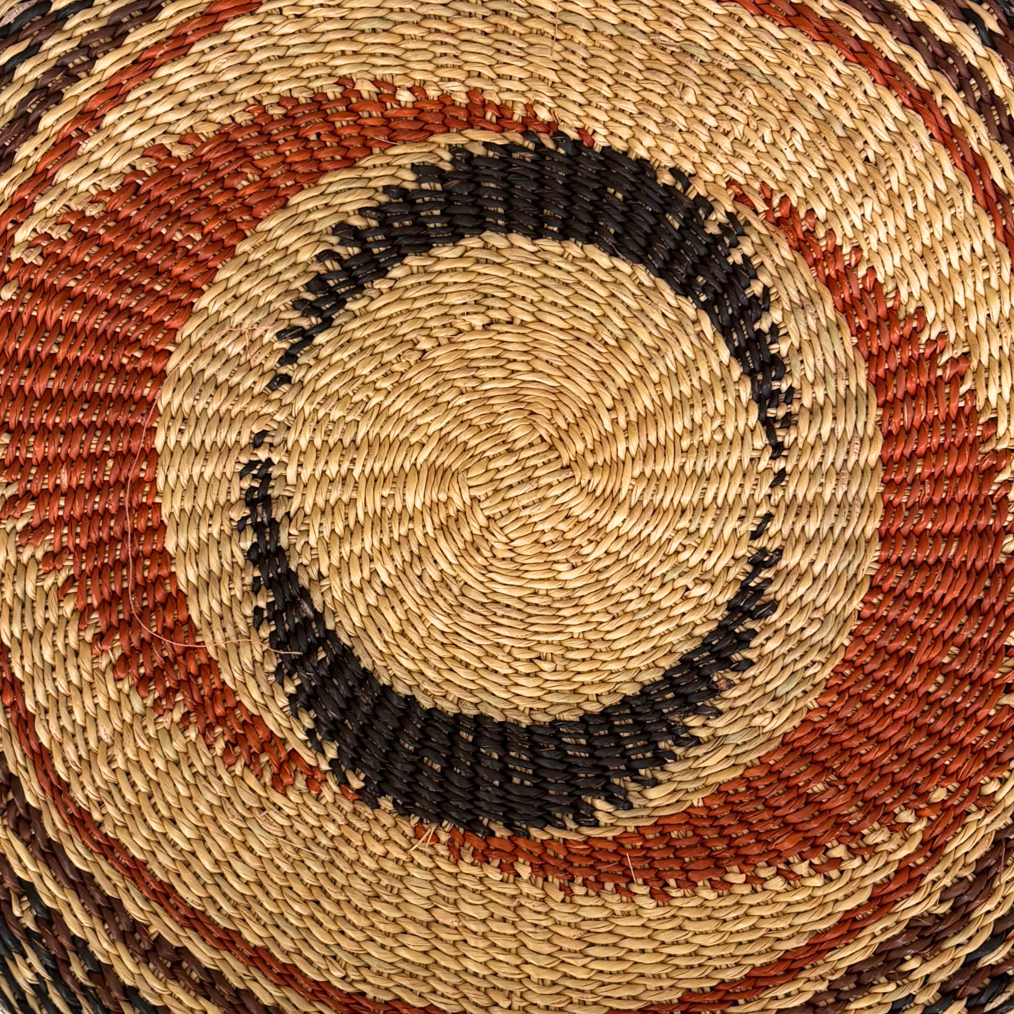 Baba Tree Placemats - Black Star Swirl. Close-up of a woven mat with concentric circle pattern in earthy tones.