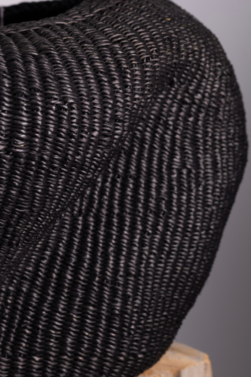 Close-up of a textured Baba Tree black woven basket on a wooden surface with a gray background