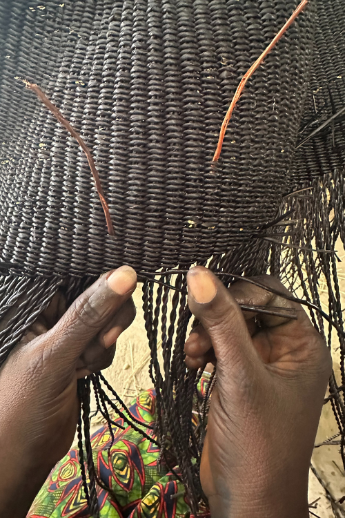 Close-up of hands weaving a baba tree black basket with a blurred background