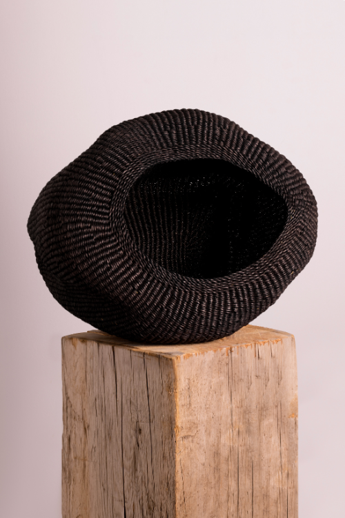 Baba Tree Black pebble basket on a wooden block with a plain background