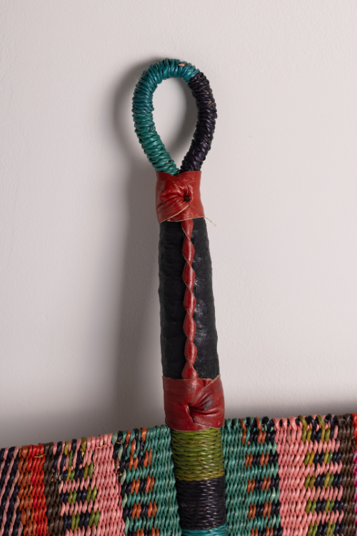 Handcrafted Bolga decorative wall fan with pink, green, and brown handle by Baba Tree, perfect for wall decor.