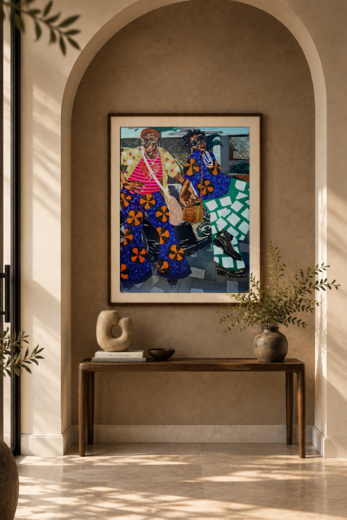A framed colorful painting named "Shakara" of two figures in patterned clothing hangs on a warm beige arched wall above a wooden console table with decorative objects and a vase.