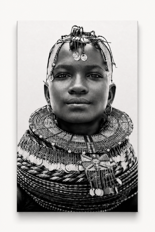 A black and white portrait canvas print of an African woman wearing elaborate beaded necklaces and head adornment, shown as a vertical rectangular artwork against a light neutral background.