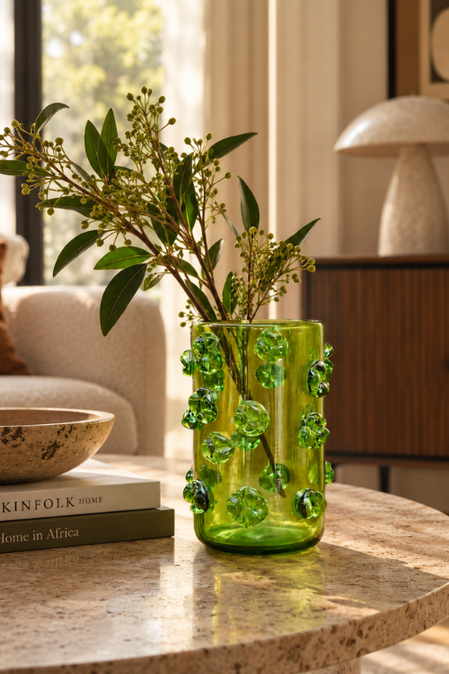 The nywele vase moss in green textured glass vase with raised bubble details, holding green foliage, styled on a marble table in a warm, sunlit living room.