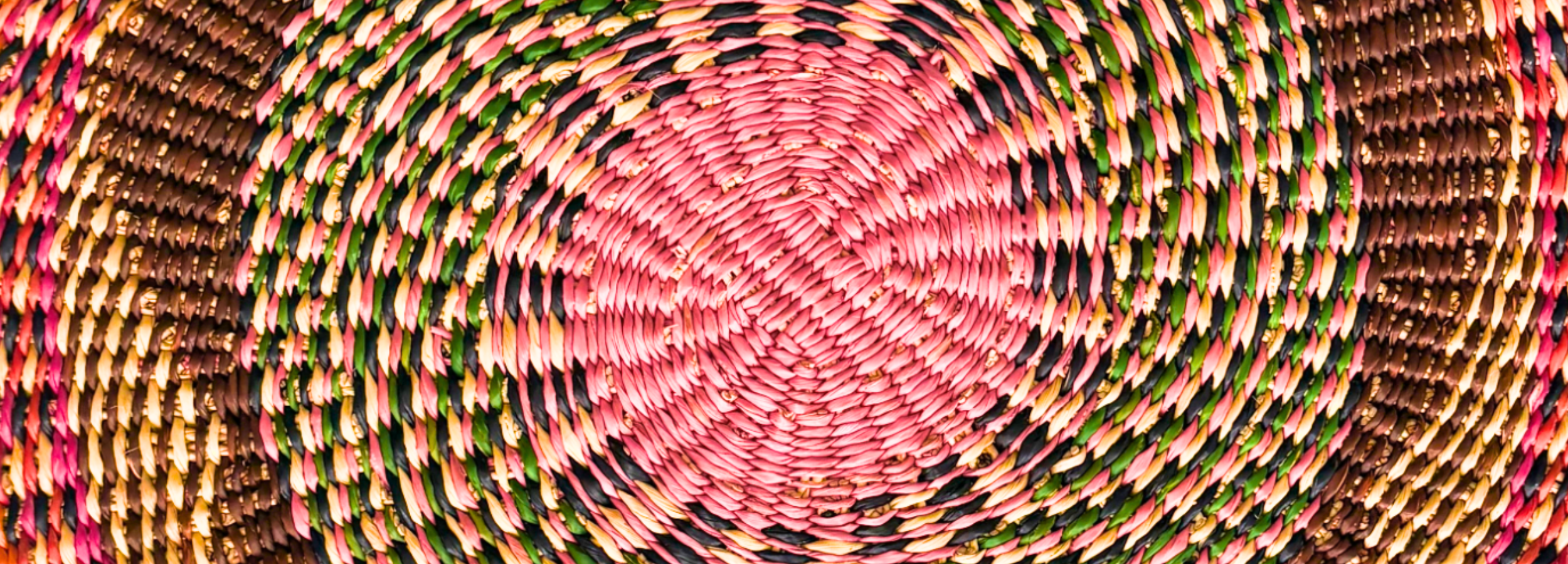 Close-up of a woven textile with concentric circular pattern in pink, green, and brown.
