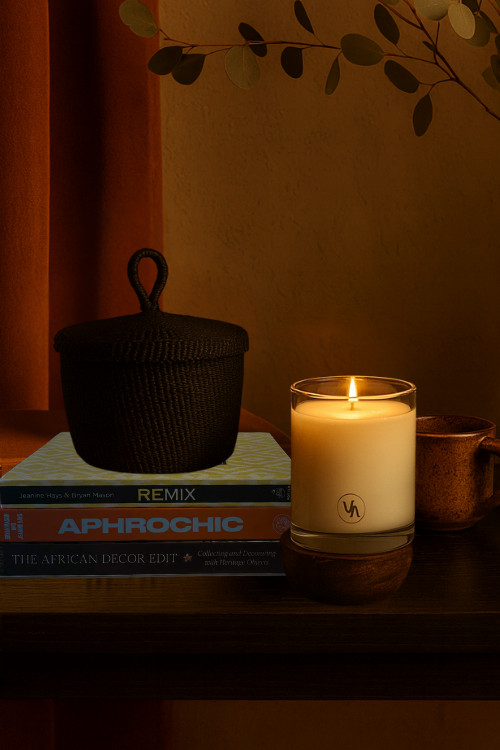 Villa Aburi Candle burning on a shelf with books and decorative items in a warm setting with Baba Tree black banasco basket.