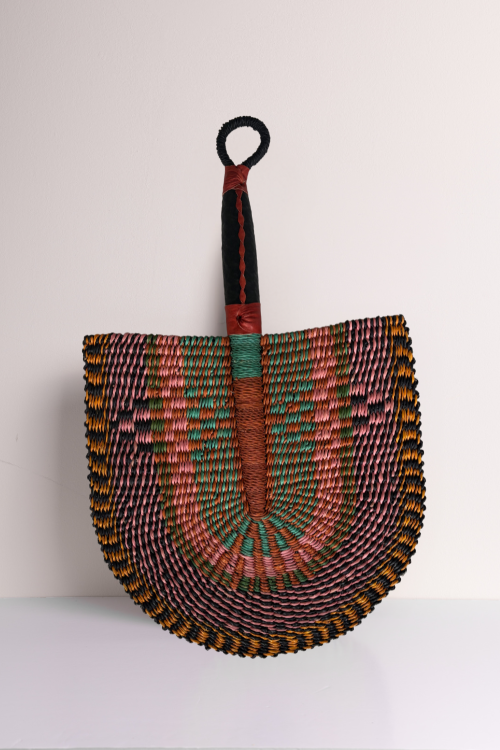 The Baba Tree Handcrafted Bolga Decorative Fan – Vibrant Mirage leaned against a white backdrop.