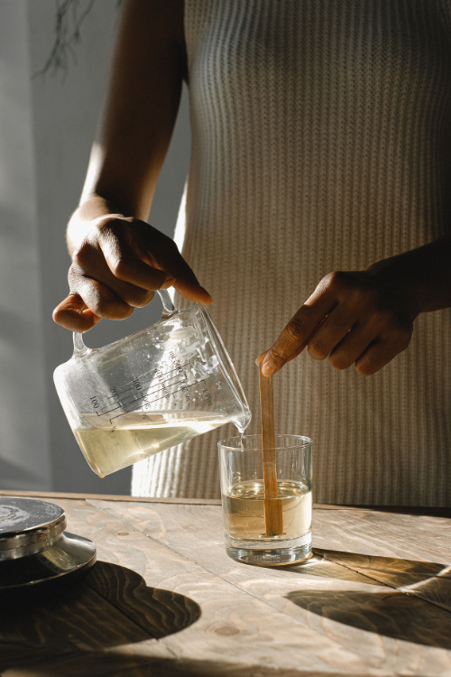 Person pouring liquid from a glass pitcher into a glass on a wooden table.