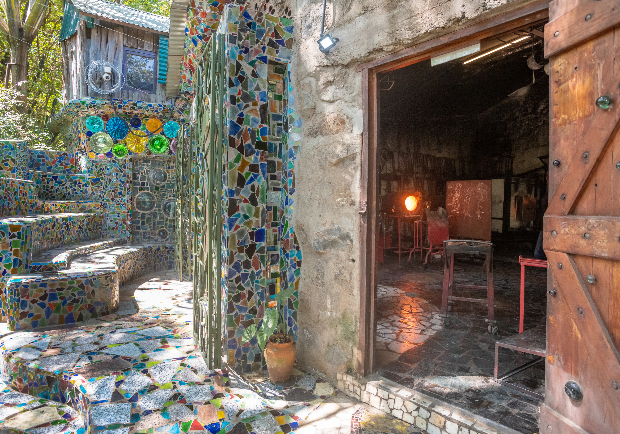 Mosaic-patterned exterior of a building with a wooden door open to reveal interior of kitengela glass workshop.