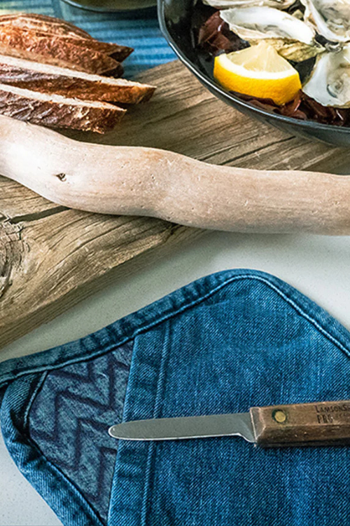 Oysters on a half shell with lemon and bread on a wooden surface, with a knife and mi cocina Denim Herringbone Quilted Trivet/Pot Holder