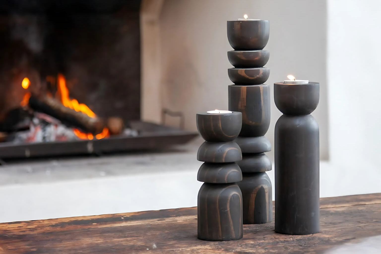 A set of 3 candle holders in small, medium and large sizes on a stool beside a bathtub in a bathroom.