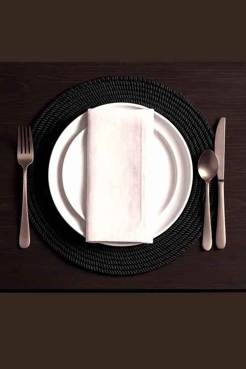 Baba Tree Dining setup with a white plate, black woven placemat, silver fork, knife, and spoon on a dark surface.