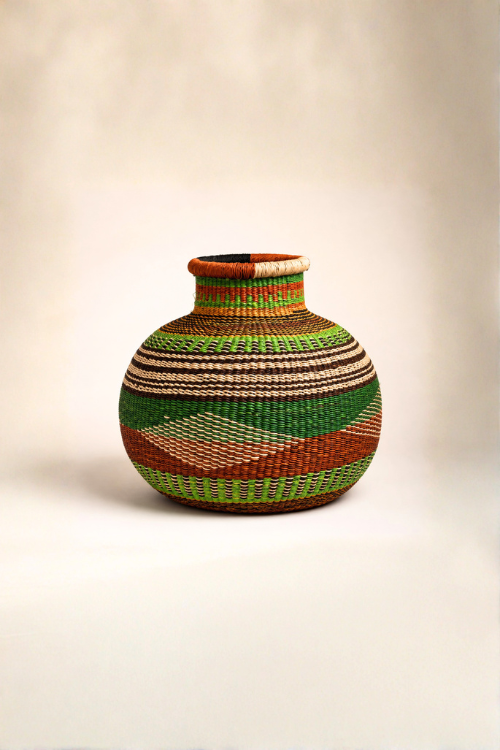 A hand-woven baba tree basket with a rounded body and short neck, decorated with geometric patterns of green, brown, beige, and orange on a neutral studio background.