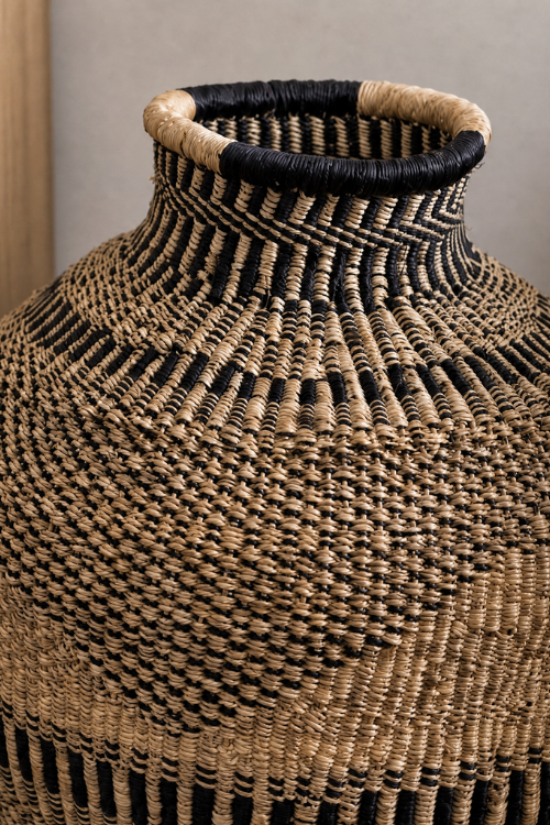 A close-up of a hand-woven Jemima 10 cows Ebony Triangle basket with a textured geometric pattern in natural tan and black, featuring a flared rim and a looped top edge.