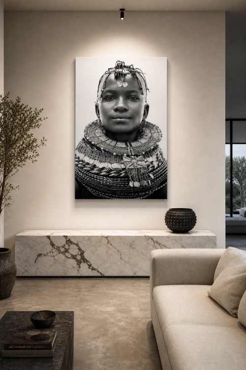 A large vertical black and white canvas print of an African portrait with intricate jewelry, displayed on a beige wall in a modern living room setting above a marble console table.