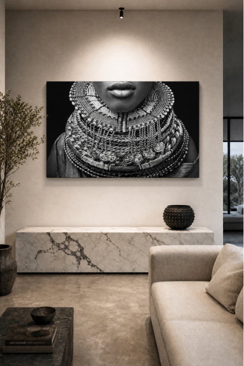 A large black and white canvas wall art print depicting a close-up of a person wearing elaborate layered necklaces, displayed in a modern living room setting above a marble console table.