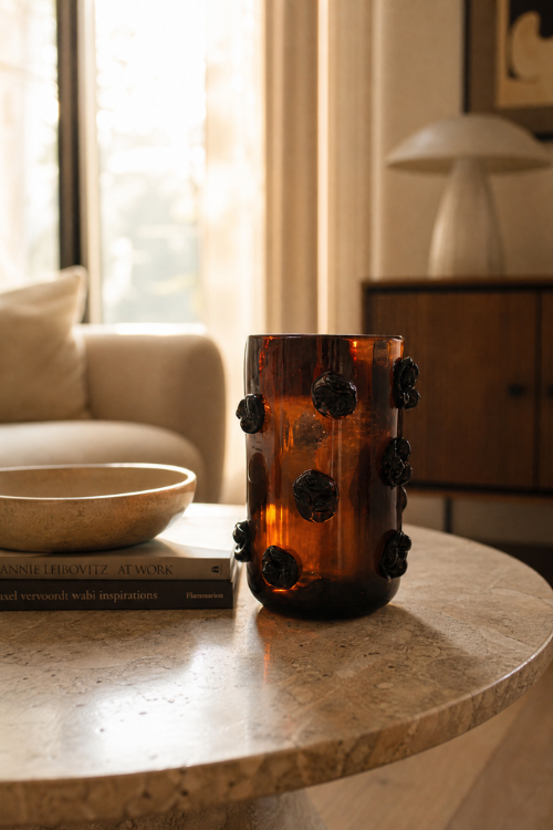 Nywele vase dark umber with black  accents sits on a round stone coffee table in a warm, modern living room setting.