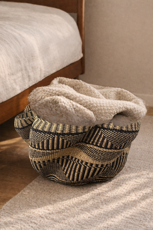 Pakurigo-Wave-Basket-Black-and-Natural-Essence with a textured blanket inside, placed on a wooden floor.