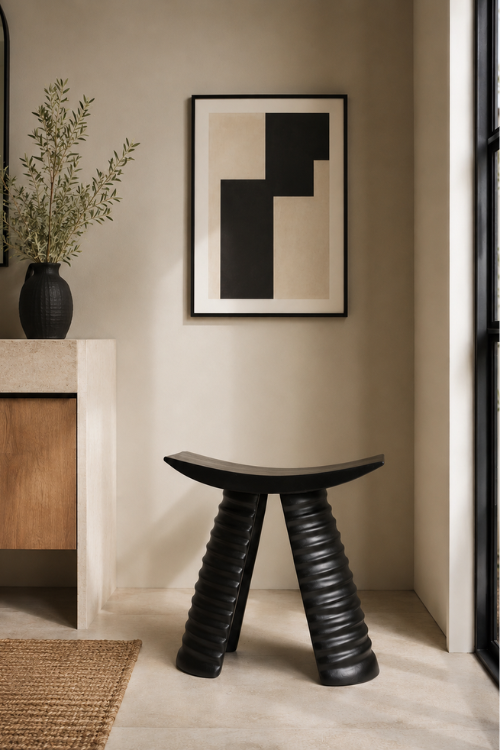 A modern sculptural black labadi ring stool with ribbed legs and a curved seat, placed in a minimalist interior setting with a framed abstract print on the wall