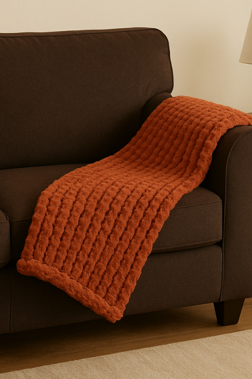 Villa Aburi Chunky Knit Blanket - Burnt Orange draped over a brown sofa against a beige wall.