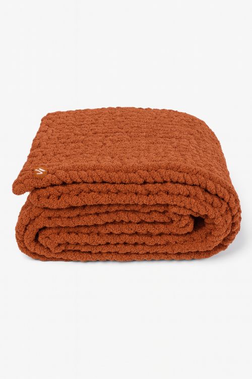 Folded Villa Aburi Burnt orange colored hand knitted throw on a white background