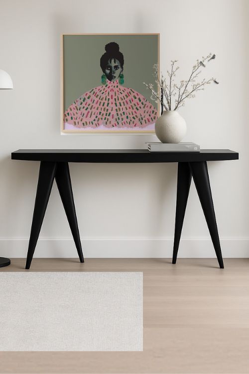 "Yagazie" Fine Art Print size 20x20. This statement piece features a confident Black woman adorned with geometric pink and green dress with green earrings against a soft green background. Walking Console in Black - Designed by Tekura placed below the art print.