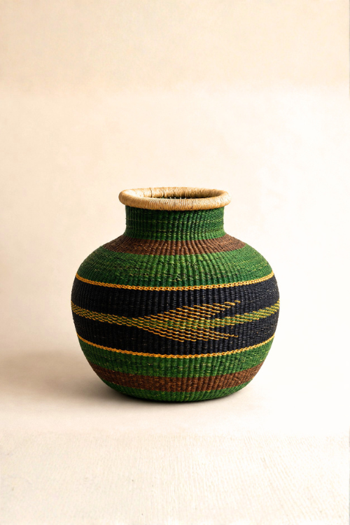 A hand-woven baba tree basket with a rounded body, a narrow neck, and a natural wood rim, decorated with horizontal stripes of green, black, brown, and yellow on a light beige background.