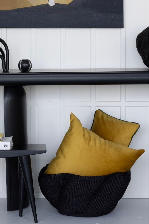 Tekura walking bench with mustard yellow Lulasclan cushions in black baba tree black pakurigo wave basket against a white paneled wall.