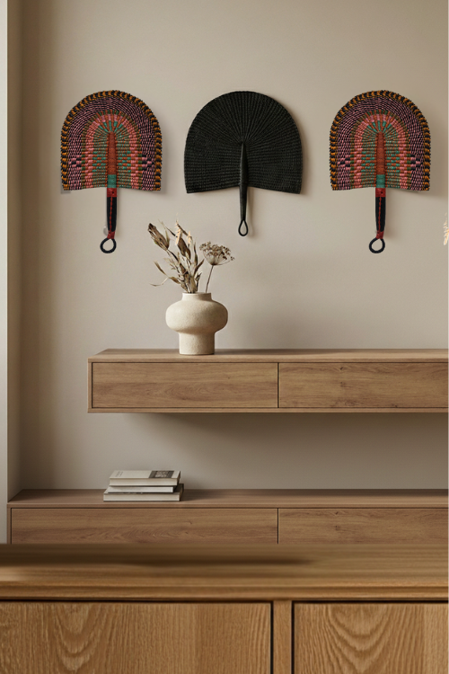 Woven bolga fans above a wooden console table with a vase and books.