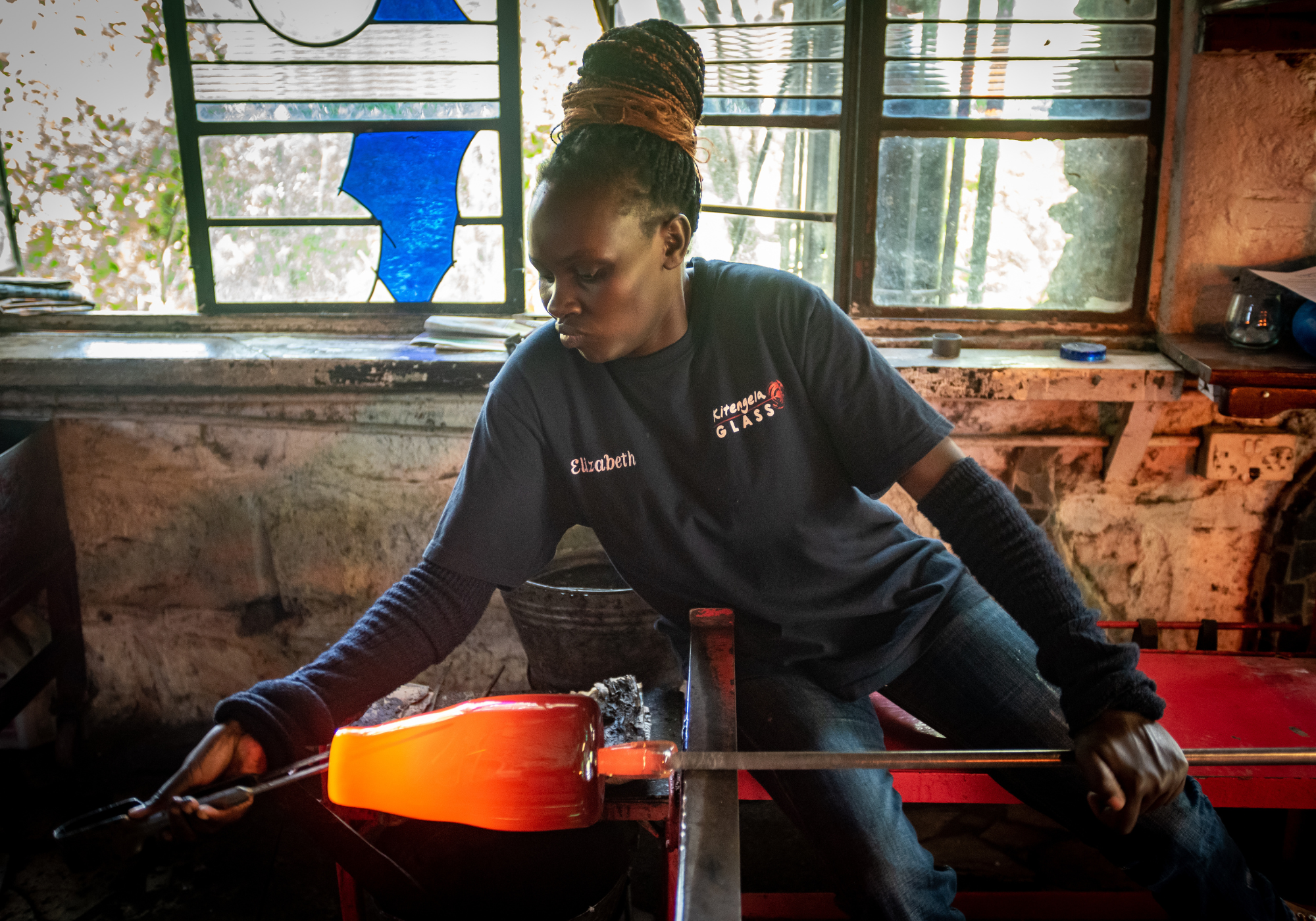 Woman artisan working with glass in a kitengela workshop setting.