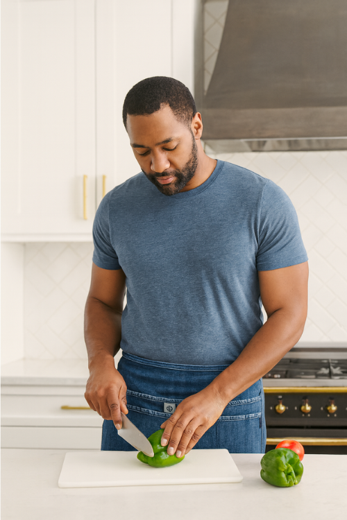 Man in a kitchen cutting a green pepper on a white cutting board wearing a mi cocina denim waist apron.